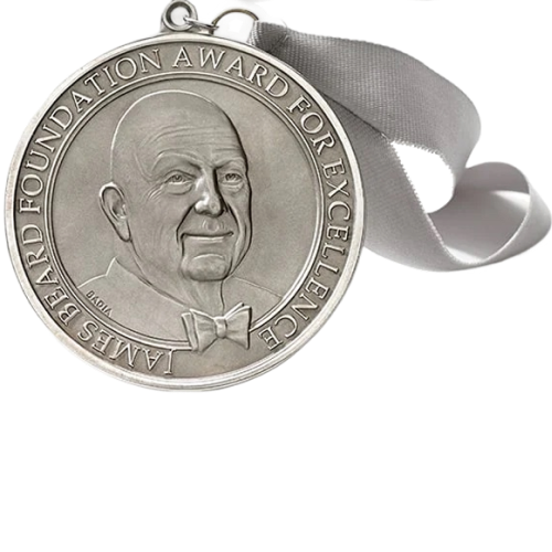 A silver James Beard Foundation Award for Excellence medal with a white ribbon.