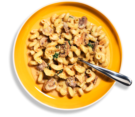 Overhead shot of Riff Creamy Parmesan Cavatappi pasta with mushrooms and spinach in a yellow bowl, with a fork resting on the side.