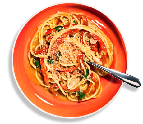 Overhead shot of Riff Coconut Curry Noodles tossed with red bell pepper strips and herbs, topped with a crumb topping, in an orange-red bowl with a fork resting on the side.
