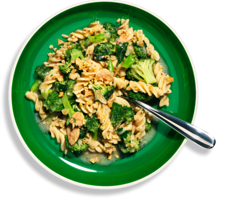 Overhead view of a green bowl of Riff Garlic Lemon Rotini pasta with broccoli and toasted breadcrumbs, with a spoon resting in it.