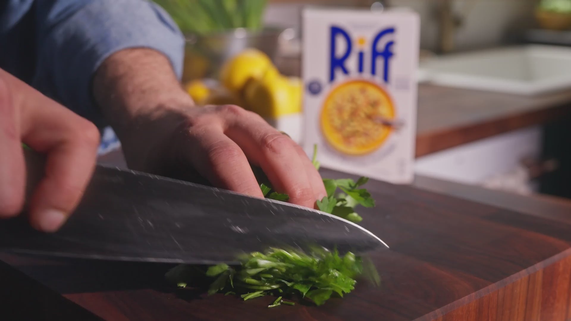 Video of a hand chopping fresh parsley on a cutting board, with lemons and a Riff Garlic Lemon Rotini box in the background.