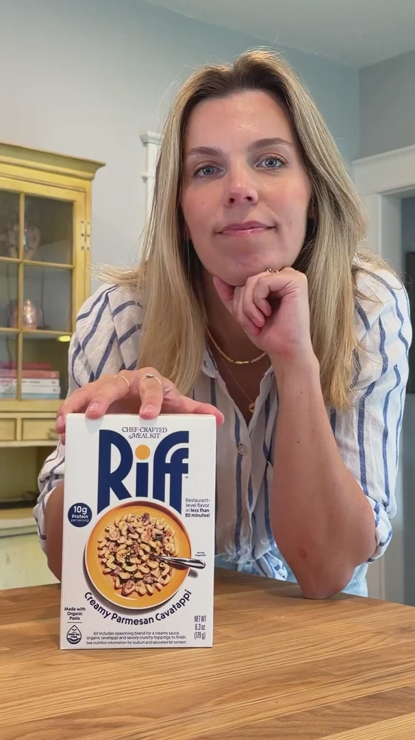 Video of a woman presenting a Riff Creamy Parmesan Cavatappi box to the camera, followed by hands stirring cavatappi pasta in a cream sauce in a yellow pan on the stove, with the box visible in the background.